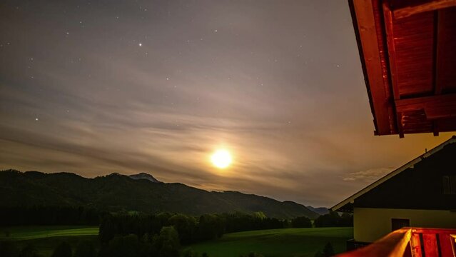Timelapse of moon setting as stars move across sky on cloudy evening