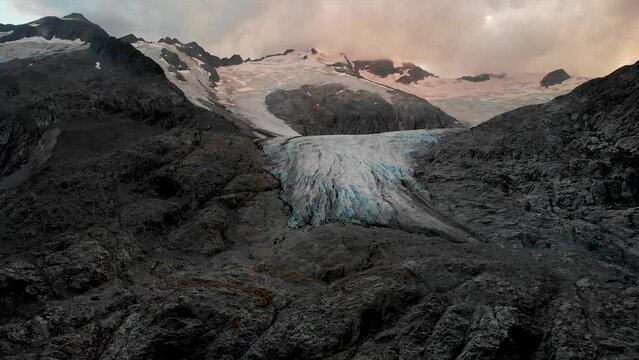 Aerial flight over the glacial lake starting with an up close view of the of  the Gauli glacier in the Bernese Oberland region of the Swiss Alps as the sun sets on a cloudy day.