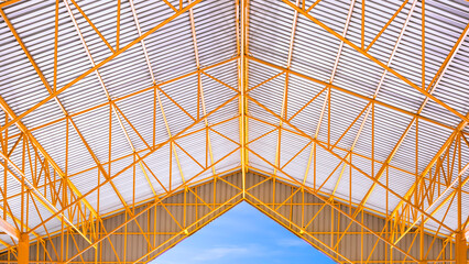 Yellow metal roof beams and aluminum corrugated tile roof of industrial building with blue sky...