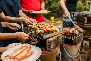 Skewers with colorful vegetables and meat grilling, family and friends gathering in the background,...