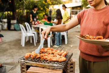 Skewers with colorful vegetables and meat grilling, family and friends gathering in the background,...