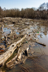 A large garbage jam blocking the riverbed with a pile of dry branches and an accumulation of plastic waste. Pollution of the environment with non-degradable waste
