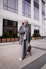 Stylish cool senior woman model in fashionable winter multilayer outfit, animal print jacket coat,...