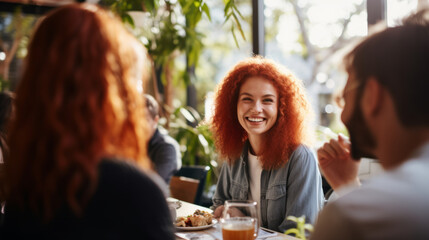 Redhead ginger caucasian business woman having a friendly lunch with colleagues at a local cafe, she engages in casual conversation, fostering a positive and collaborative atmosphere - obrazy, fototapety, plakaty