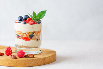 Parfait in a glass with berries, mint, whipped cream and biscuit on a wooden board. Healthy food,...