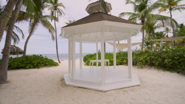 Classic white wedding altar next to a paradisiacal beach with palm trees and the sea.