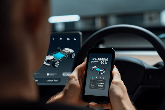 Electric car driver checks battery charging status, range and charging limit on app screen in the car. Smart technology device show EV car recharging data of electric storage in car battery innards.