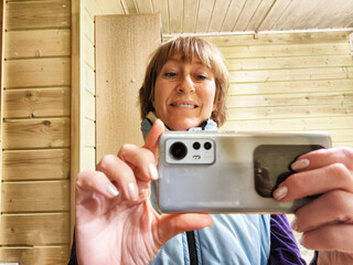 Middle-aged woman using smartphone for selfie and blogging. A female blogger poses in a photo. The...