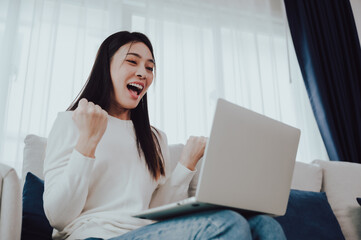 Funny euphoric young asian woman celebrating winning or getting ecommerce shopping offer on computer laptop. Excited happy girl winner looking at notebook celebrating success