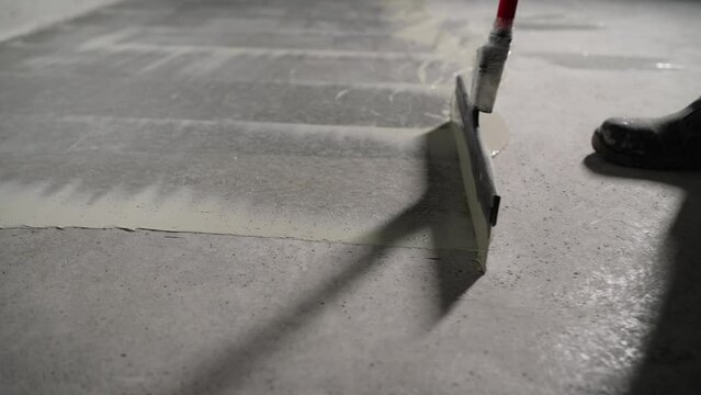 The process of priming a floor with a solution. Waterproofing concrete floor. Industrial primer. The process of priming the floor with a liquid solution using a spatula.