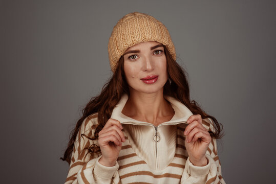 A beautiful girl wearing a beige large-knit hat and sweater on a gray background. Place for text. Winter stylish image