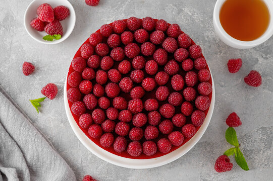 No baked raspberry cheesecake or raspberry cream mousse cake with jelly and fresh berries on top on a white plate on a gray concrete background. Summer cake.