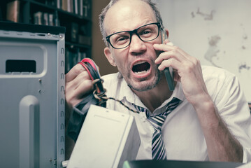 Furious hot-tempered man having problem with office computer, talking with tech support and yelling, In an office scene, a man repairs a computer, manifesting nervousness and low spirits