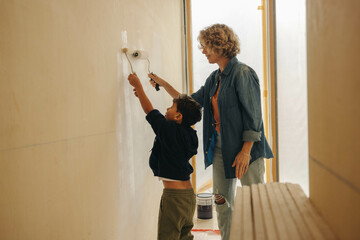 Family bonding through home renovation: Mother and son painting together on indoor wall