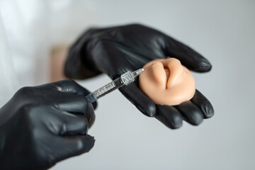 a close-up of a hand with a syringe is practicing stabbing at mouth silicone lips for practice skin