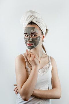 Young womanin white towel applying mud black mask on her face isolated on white, spa treatment