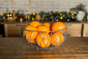 Fresh tangerines in Metal bowl on table against stylish decorated christmas tree with golden lights in scandinavian room. Atmospheric winter holidays at festive home.new year celebration