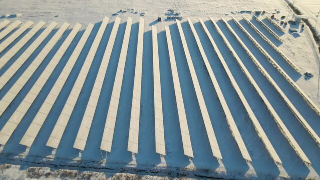 Aerial view of sustainable electrical power plant with solar photovoltaic panels covered with snow in winter for producing clean energy. Concept of low effectivity of renewable electricity in north