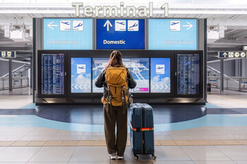 Young Asian woman in international airport looking at flight information board, checking her flight - obrazy, fototapety, plakaty