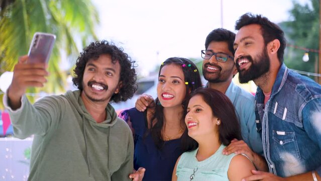 Group of friends talking on video call or chat during evening party gathering on terrace - concept of smartphone communication, virtual meetup and technology