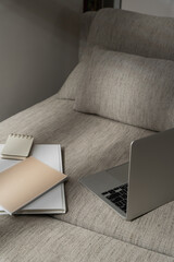 Laptop computer and office documents on comfortable sofa with sunlight shadows. Work at home concept