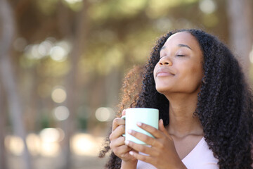 Black woman smelling coffee from cup in a park