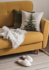 A cozy corner of the living room - a yellow armchair with pillows, a plaid, fluffy slippers on the...