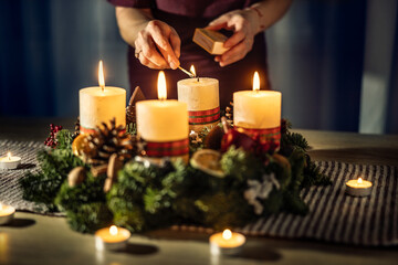 A woman lights the last fourth candle on an Advent wreath during Christmas Eve - Powered by Adobe