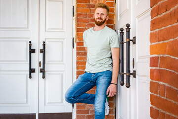 Portrait of Smiling Young Redhead bearded Man with red Facial Hair standing at old Brick Wall.Sunny...
