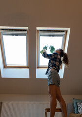 Woman cleans skylight window in her apartment. Housework, cleaning roof windows at home.