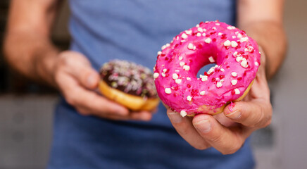 Pink donut with sprinkles in male hand close-up.