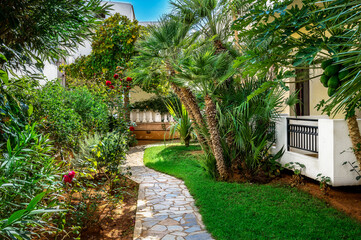 Fototapeta premium A tropical haven unfolds as a garden nestles next to the house, featuring lush Mediterranean plants. Ideal for travel brochures, gardening magazines and for projects seeking the perfect harmony.