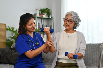 Asian caregiver helping senior female patient exercise with dumbbells at home