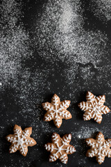 Obraz na płótnie Canvas Black table background with flour and star gingerbread cookie decorated with sugar glaze, top view, copy space