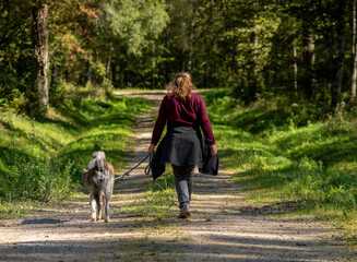 dame marchant avec son chien en laisse dans un chemin forestier