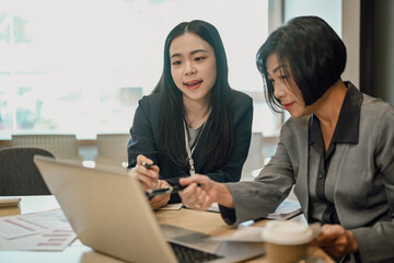 Senior female ceo and young female worker discussing company presentation at meeting table