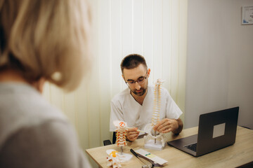 Aging and back pain concept: doctor of rheumatolgy showing her senior patient a slipped disk on a backbone model.