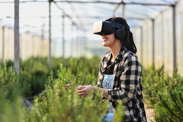 Cheerful female farmer with VR headset for analyzing and controlling plants quality in greenhouse