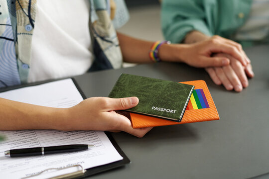 Close-up of lesbian couple giving passports to get married while filing documents and having meeting with consultant
