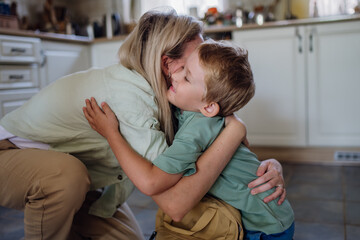 Mother saying goodbyeto to son before school, hugging, embracing him in kitchen.