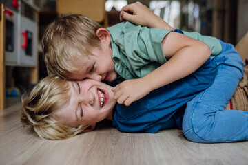 Obraz na płótnie Canvas Two little boys fighting on the floor, brothers having fun at home. Concept of sibling relationship and brotherly love.