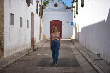 Young woman, blonde, green eyes, wearing pink top and jeans, walking along a lonely street of a...