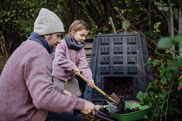 Girl helping father to remove compost from a composter in garden. Concept of composting and...