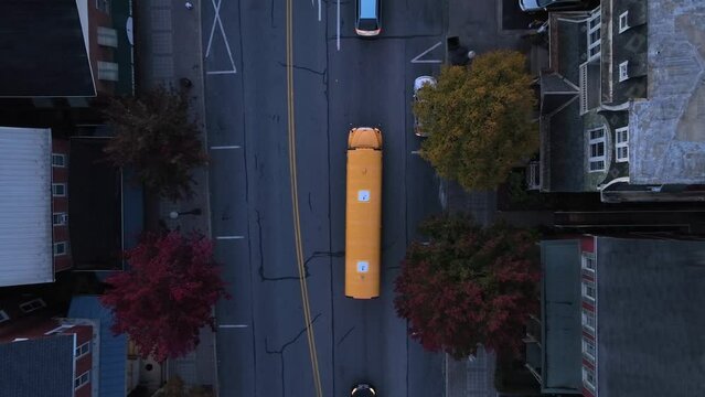 Yellow school bus in small town America during autumn morning. Aerial top down rising shot of USA school transportation.