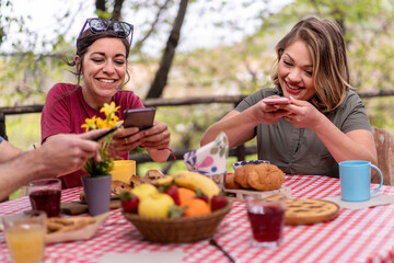 Two women enjoy capturing their vibrant brunch setup on smartphones, indulging in the foodie culture.