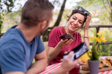 Woman laughing joyfully as she shares content on her smartphone with a friend during an outdoor gathering.