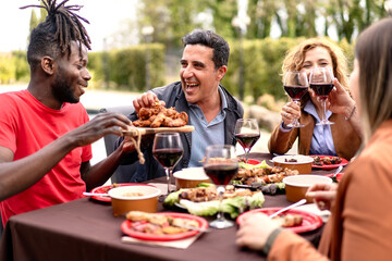 Friends of diverse ethnicities share a laugh over a sumptuous outdoor meal food, toasting with...