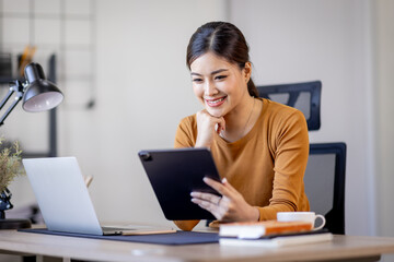 Young modern business asian woman working using digital tablet while sitting in the home office