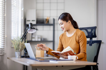 freelancer asian woman writing on a notebook while working on laptop computer in home office