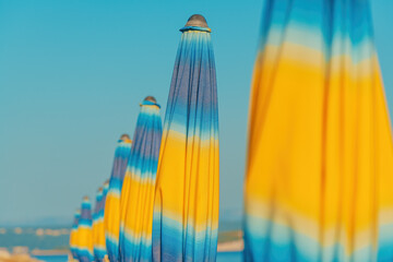 Folded colorful beach umbrella parasols on Adriatic sea coast in sunny summer morning, holiday and...